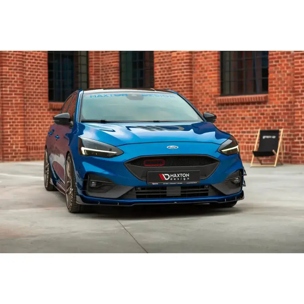 Frontspoiler på Ford Focus Mk4 St-Line, blå bil med svarte detaljer foran rød murvegg.