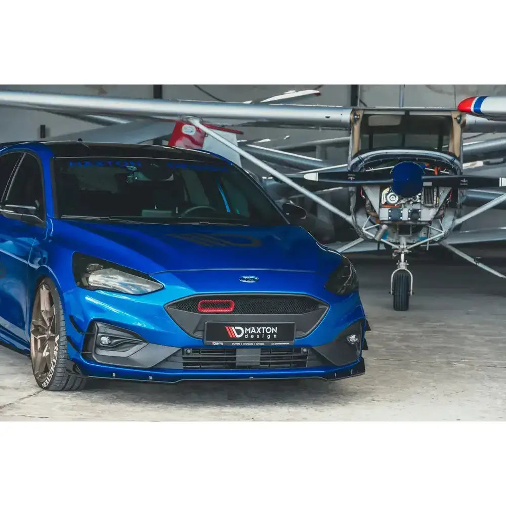 Front splitter på blå Ford Focus Mk4 St-Line sett forfra i garasje med småfly i bakgrunnen.