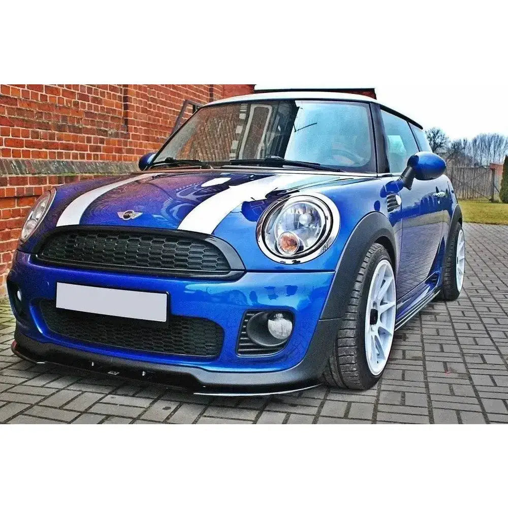 Frontsplitter på blå Mini Cooper R56 Jcw med hvite striper og felger, parkert ved mursteinsvegg.