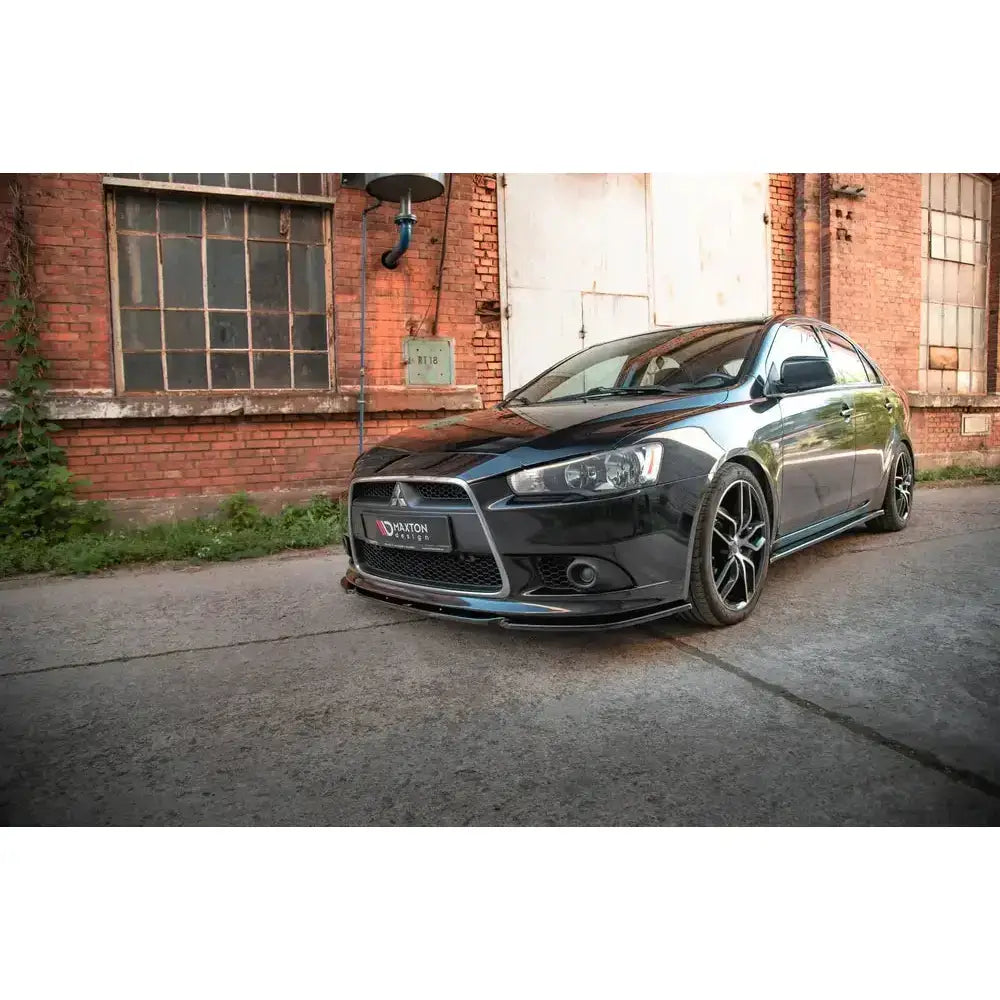 Frontsplitter på Mitsubishi Lancer Sportback Mk8 med store felger, lav vinkel, parkert foran mursteinsbygning.