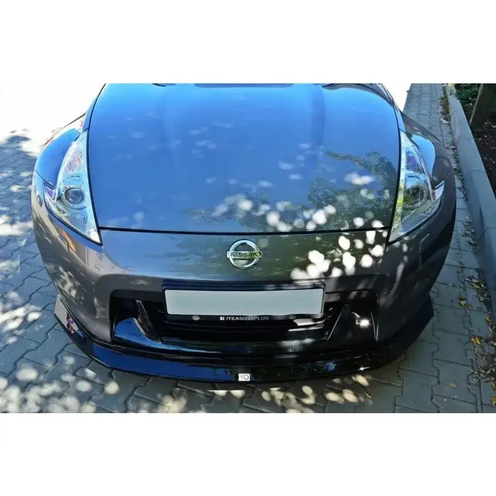 Frontsplitter til Nissan 370Z, blank svart spoiler montert foran på grå bil med synlig emblem.