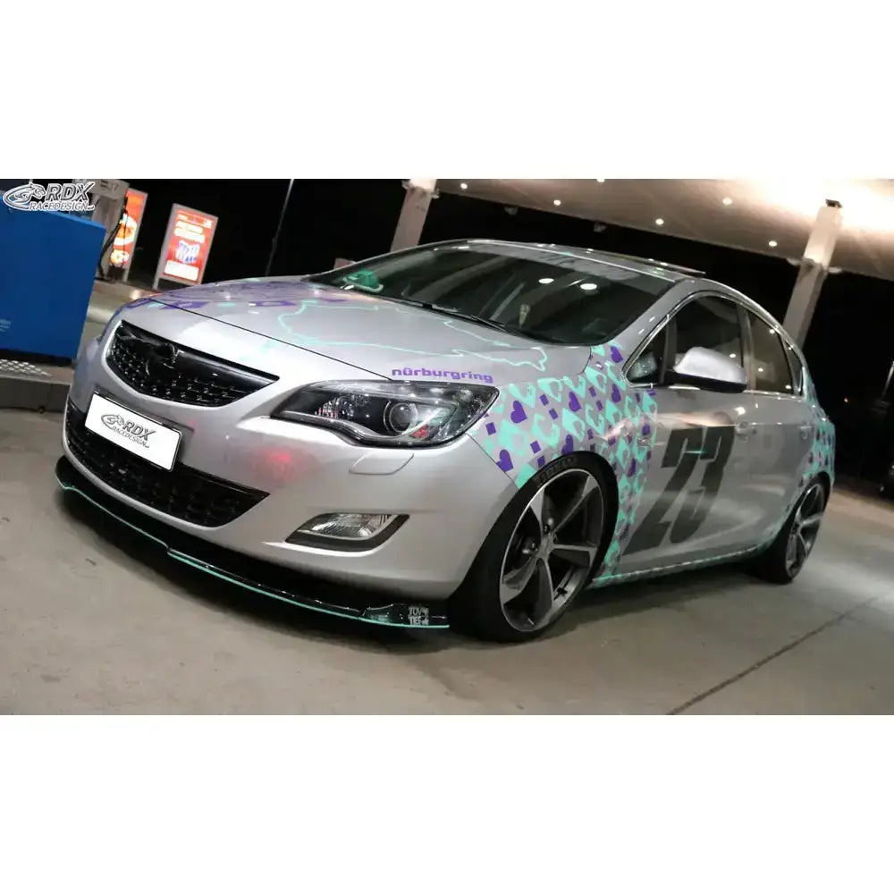 Frontsplitter Opel Astra J med sølvfarge, racing-dekor og nummer 23 ved bensinstasjon.