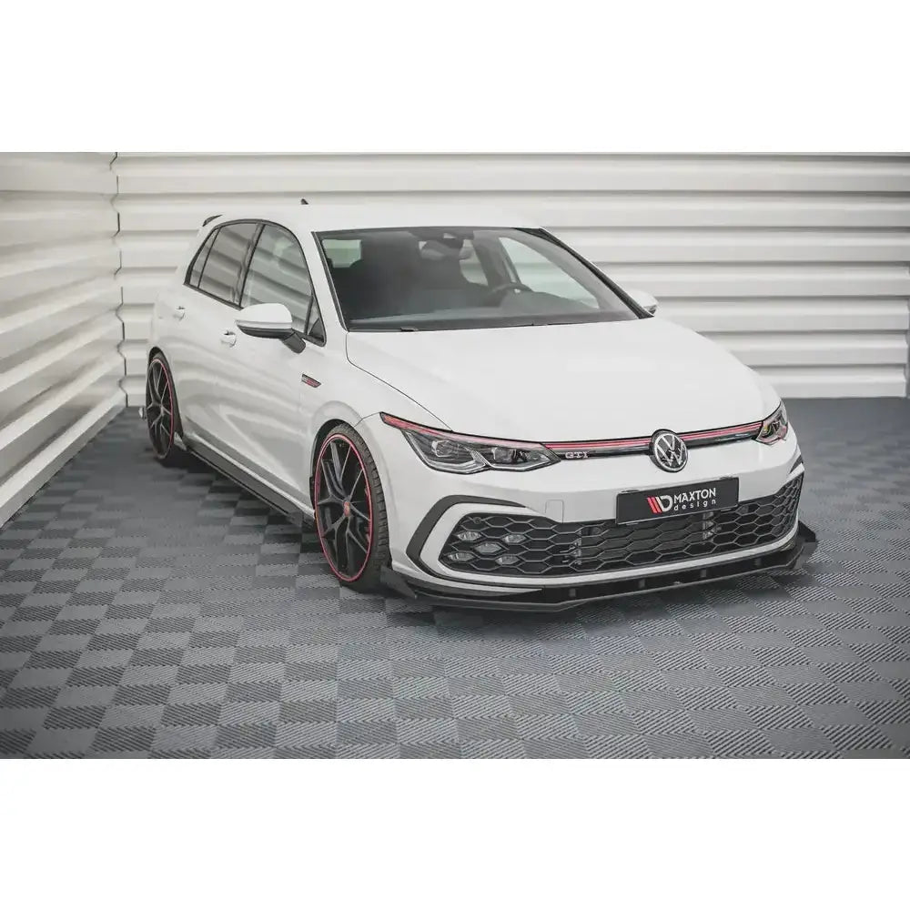 Front lip på Volkswagen Golf 8 GTI med sorte felger og røde detaljer, parkert innendørs.