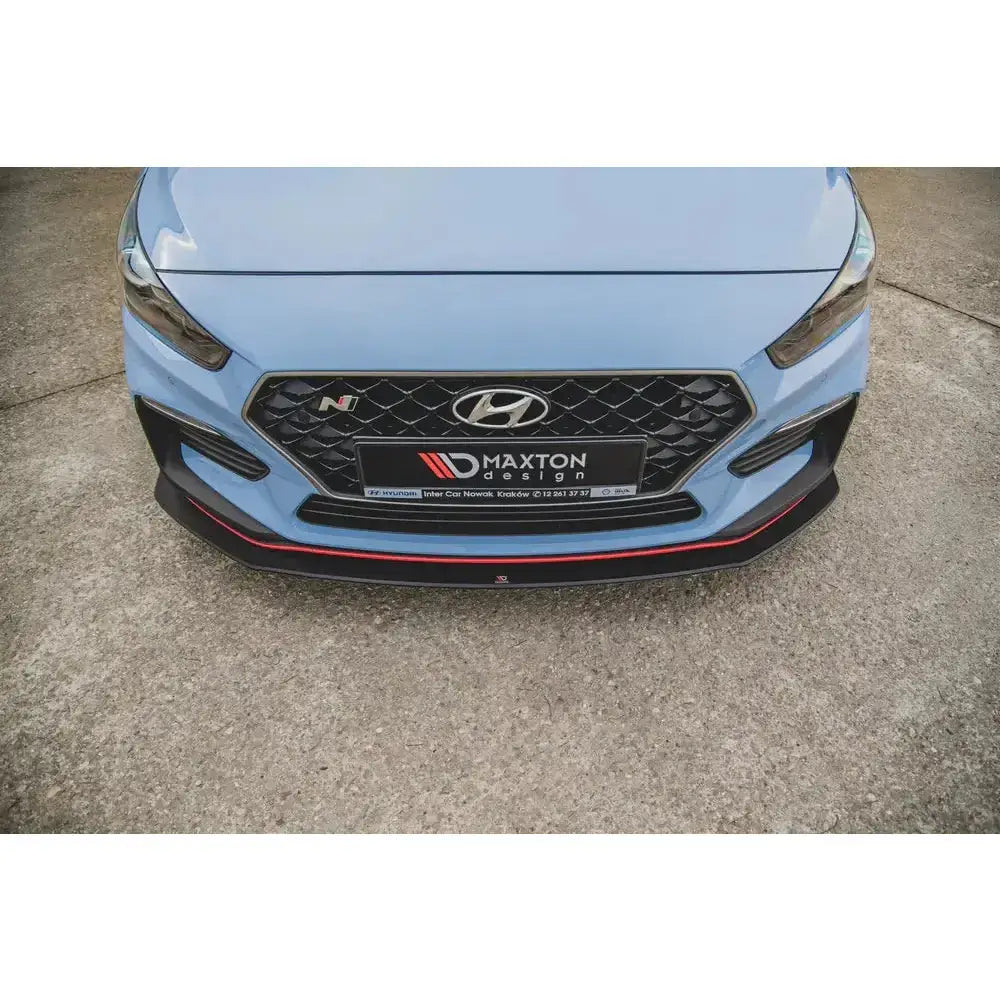 Frontsplitter på Hyundai I30 N Mk3 med sort grill og rød dekorlinje, fotografert rett forfra utendørs.
