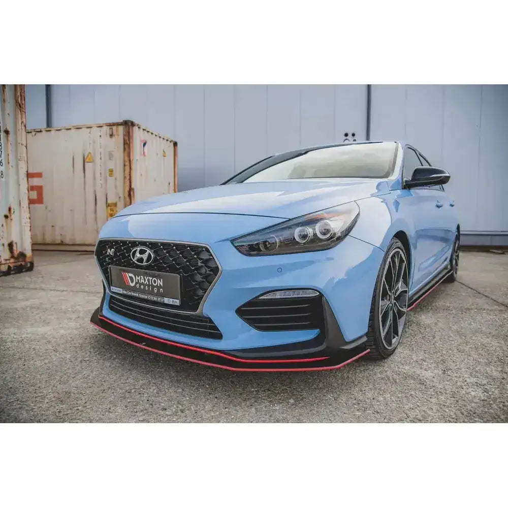 Front lip på Hyundai I30 N Mk3 med svart og rød splitter, store felger og parkeringsplass i bakgrunnen.