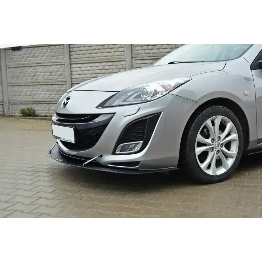 Frontleppe Racing Mazda 3 Mk2 Sport montert på sølvfarget bil med metallstag, foran brostein og betongvegg.