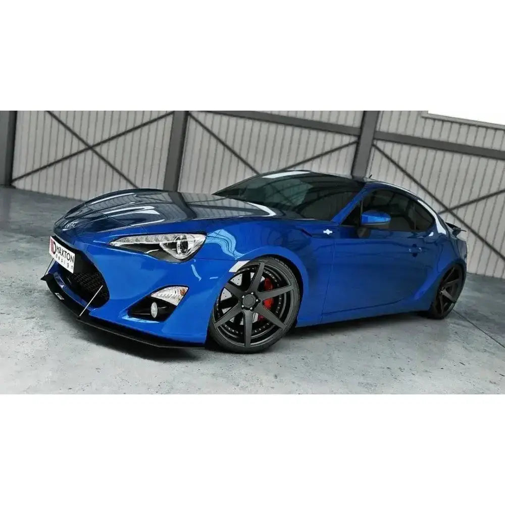 Frontsplitter på blå Toyota GT86 med store mørke felger og røde bremsekalipere i industrihall.
