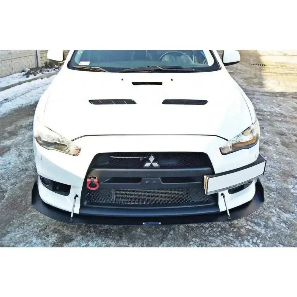 Frontsplitter Racing V.1 på hvit Mitsubishi Lancer Evo X med rødt slepeøye og metallstøtter utendørs.