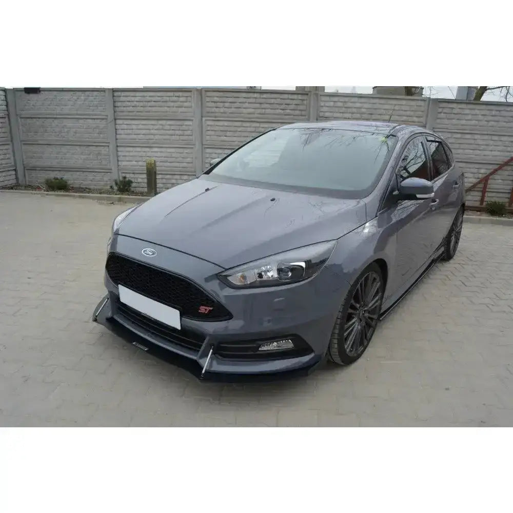Frontspoiler på grå Ford Focus 3 ST Facelift med svarte felger, parkert foran murvegg.