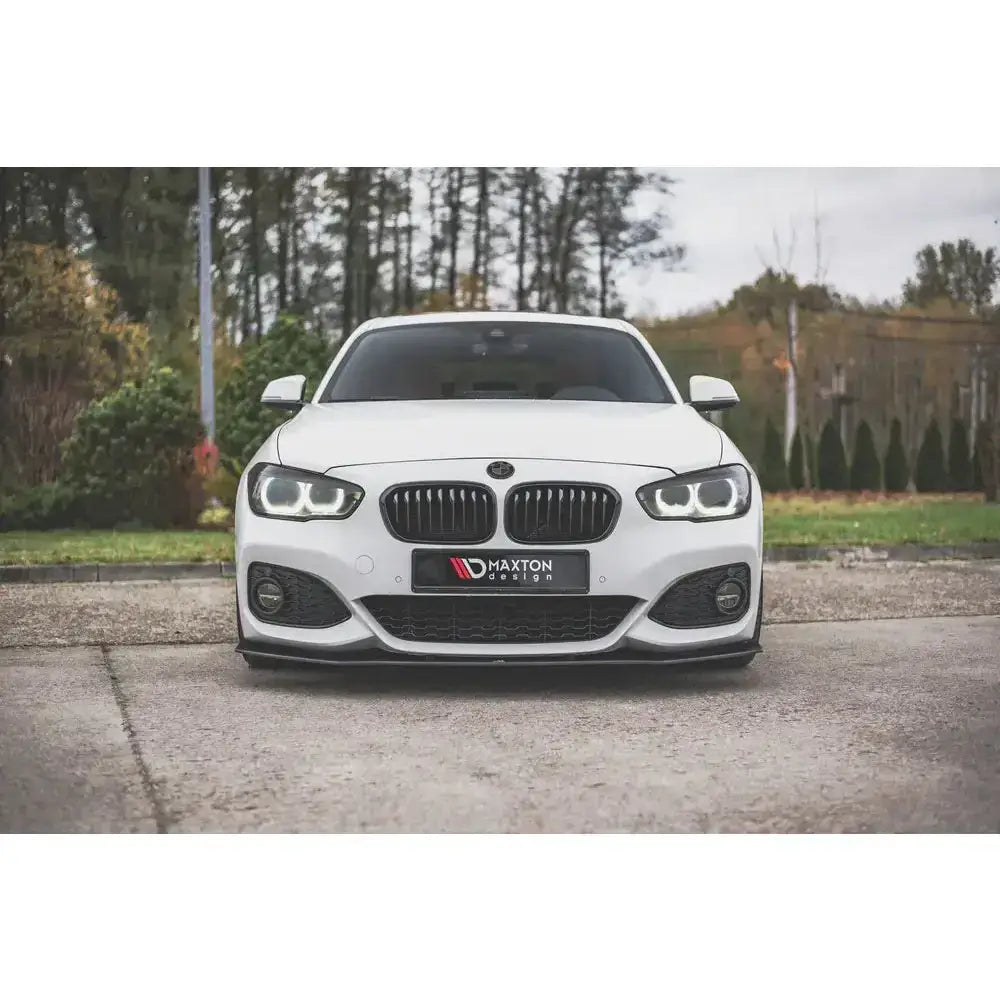Front lip på hvit BMW 1 F20 M-Pack Facelift med sort spoiler, sett forfra, parkert utendørs.