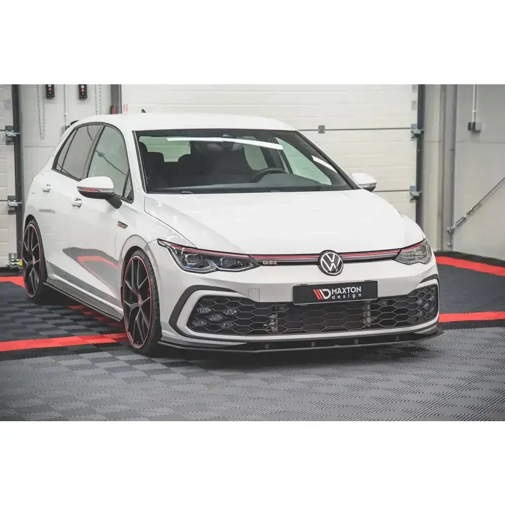 Frontspoiler på hvit Volkswagen Golf 8 GTI med sorte og røde detaljer, fotografert innendørs.