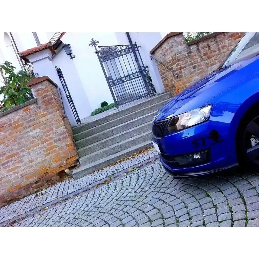 Frontsplitter på blå Skoda Rapid med svart dekor, parkert ved brosteinsgate og smijernsport.