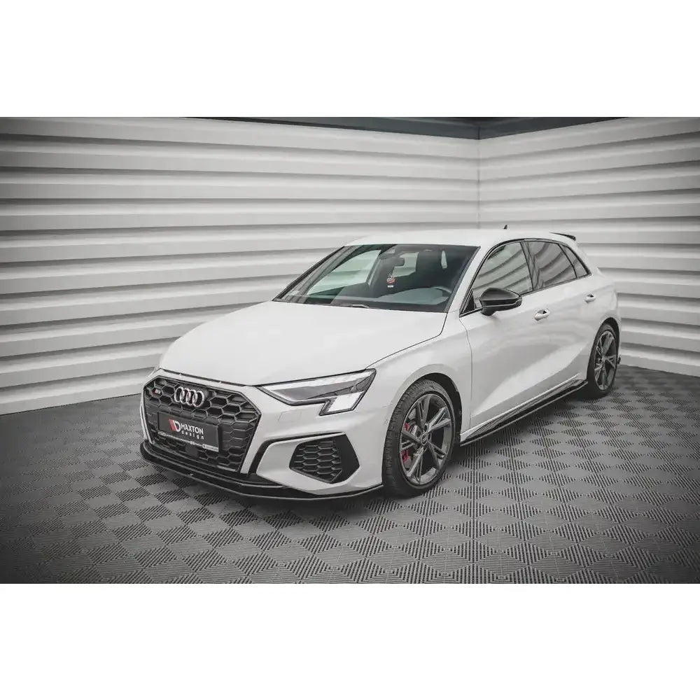 Frontspoiler på hvit Audi S3 med sorte felger, fotografert innendørs på sjakkmønstret gulv.
