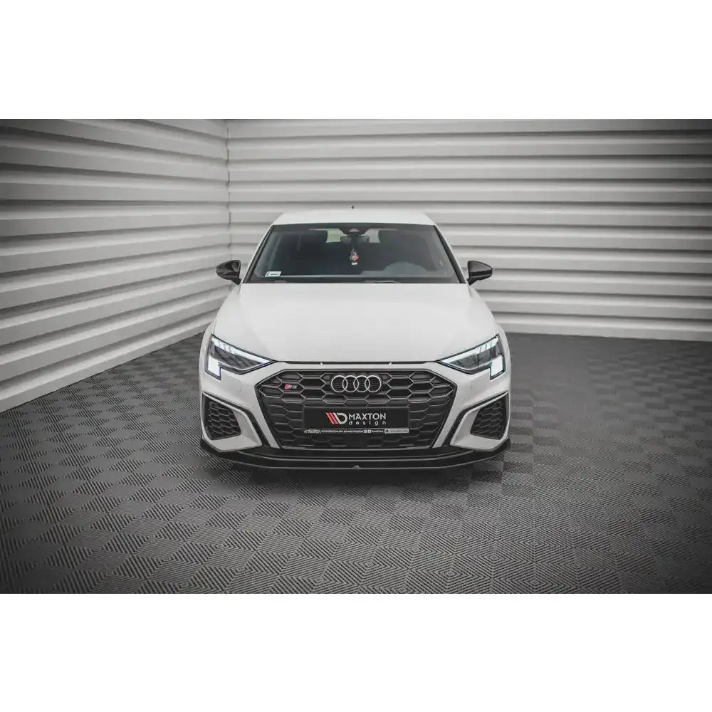 Frontsplitter på hvit Audi S3 med sort grill og LED-lys, fotografert forfra i rom med grå vegger.