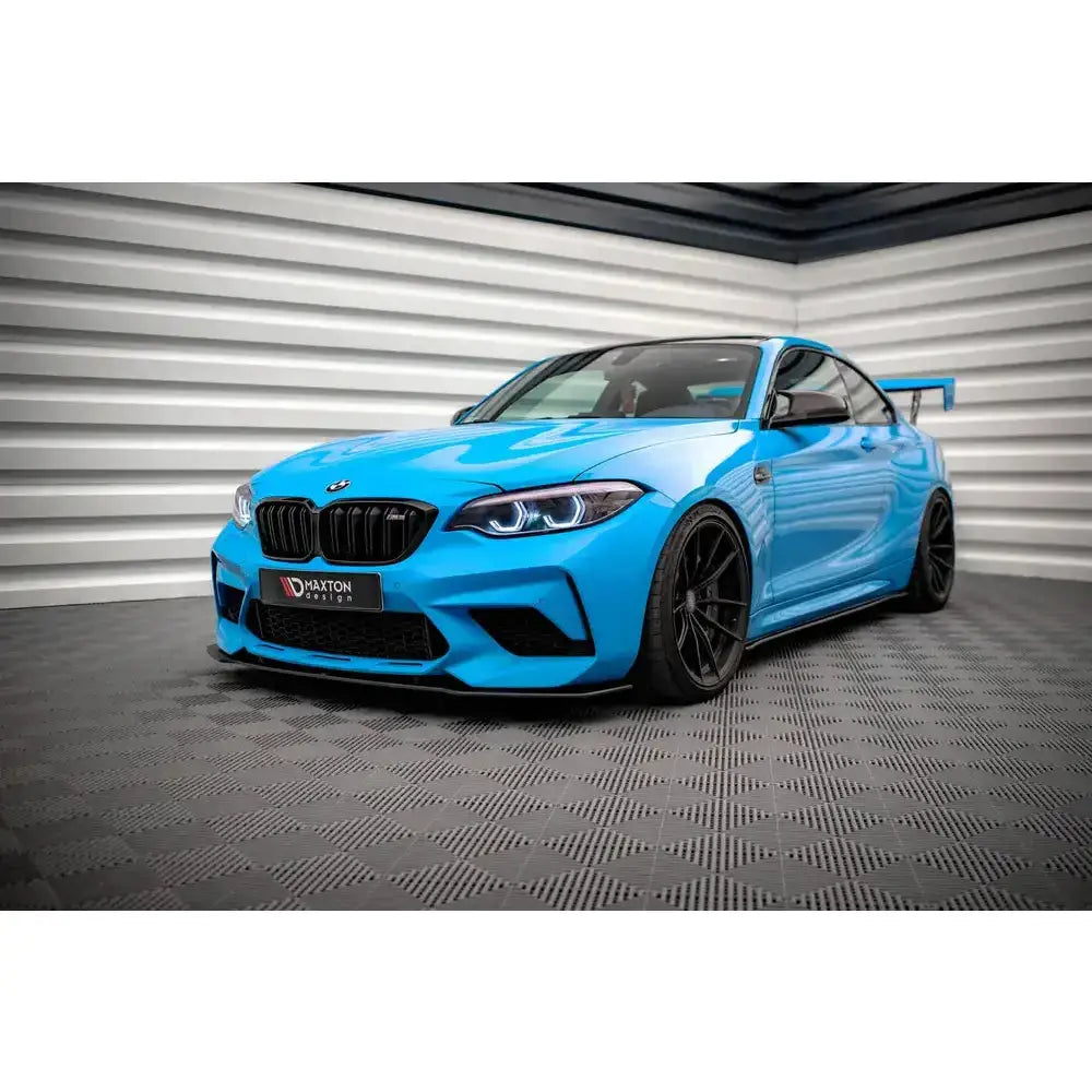 Frontspoiler på blå BMW M2 Competition F87 med svarte felger og stor bakvinge, sett fra siden.