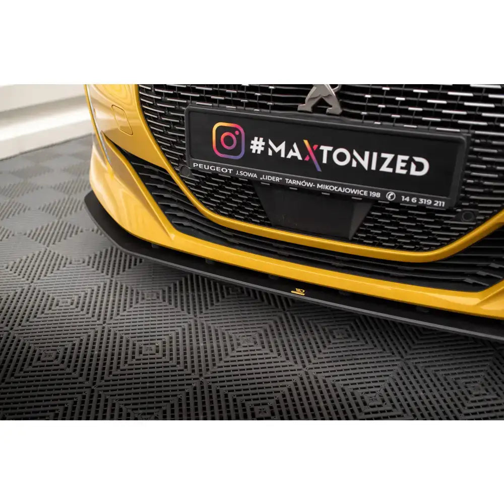 Front lip på Peugeot 208 GT Mk2 med sort splitter mot gul bil og sort grill på mønstret underlag.