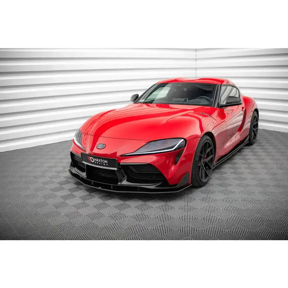 Frontsplitter på rød Toyota Supra Mk5 med svarte felger, fotografert skrått forfra i lyst rom.