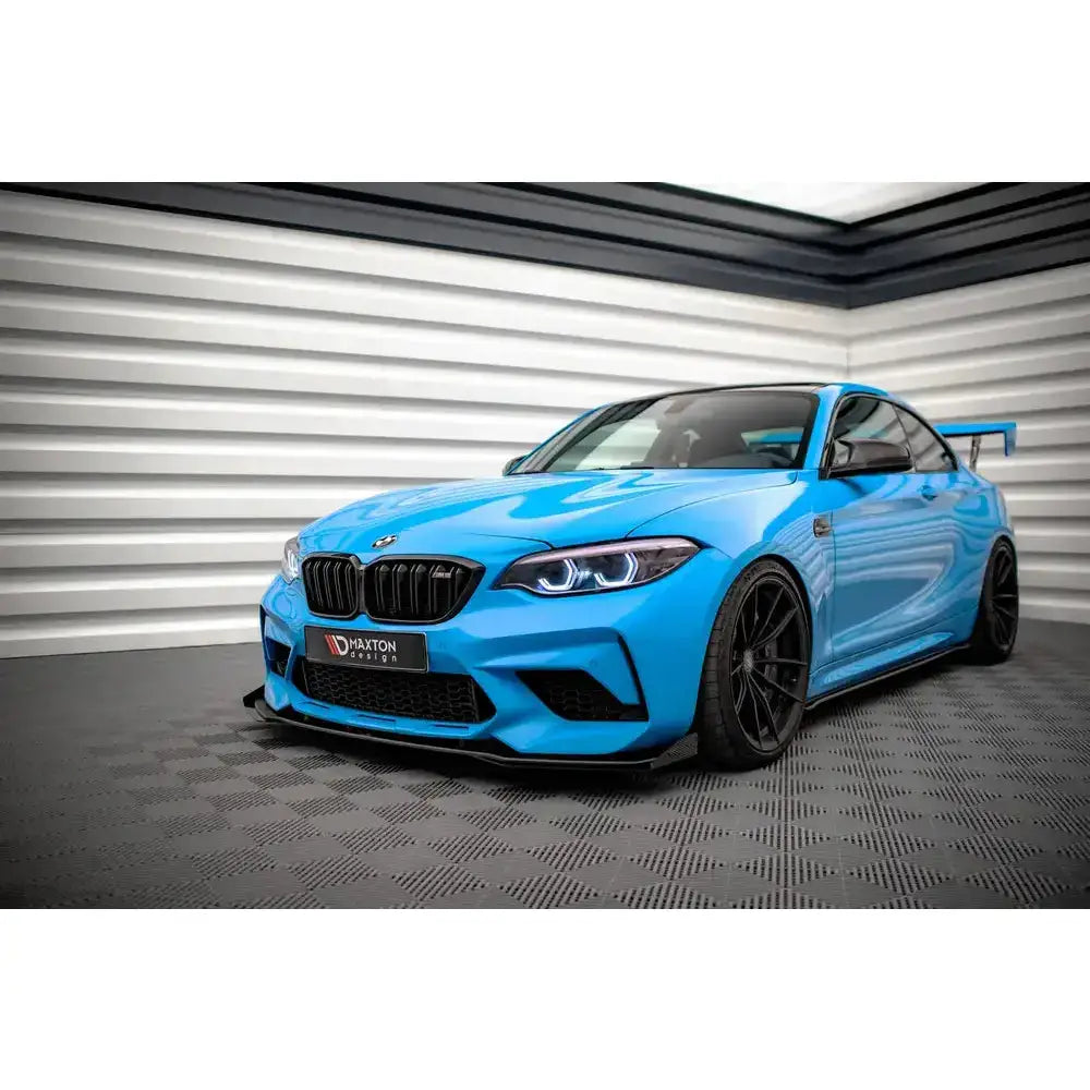 Front lip på Bmw M2 Competition F87 med sorte felger og markant hekkspoiler, parkert innendørs.