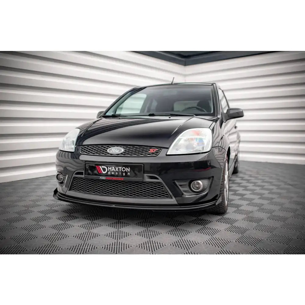 Frontspoiler Street Pro V1 med flaps på Ford Fiesta ST Mk6, sett forfra mot stripete vegg og rutet gulv.