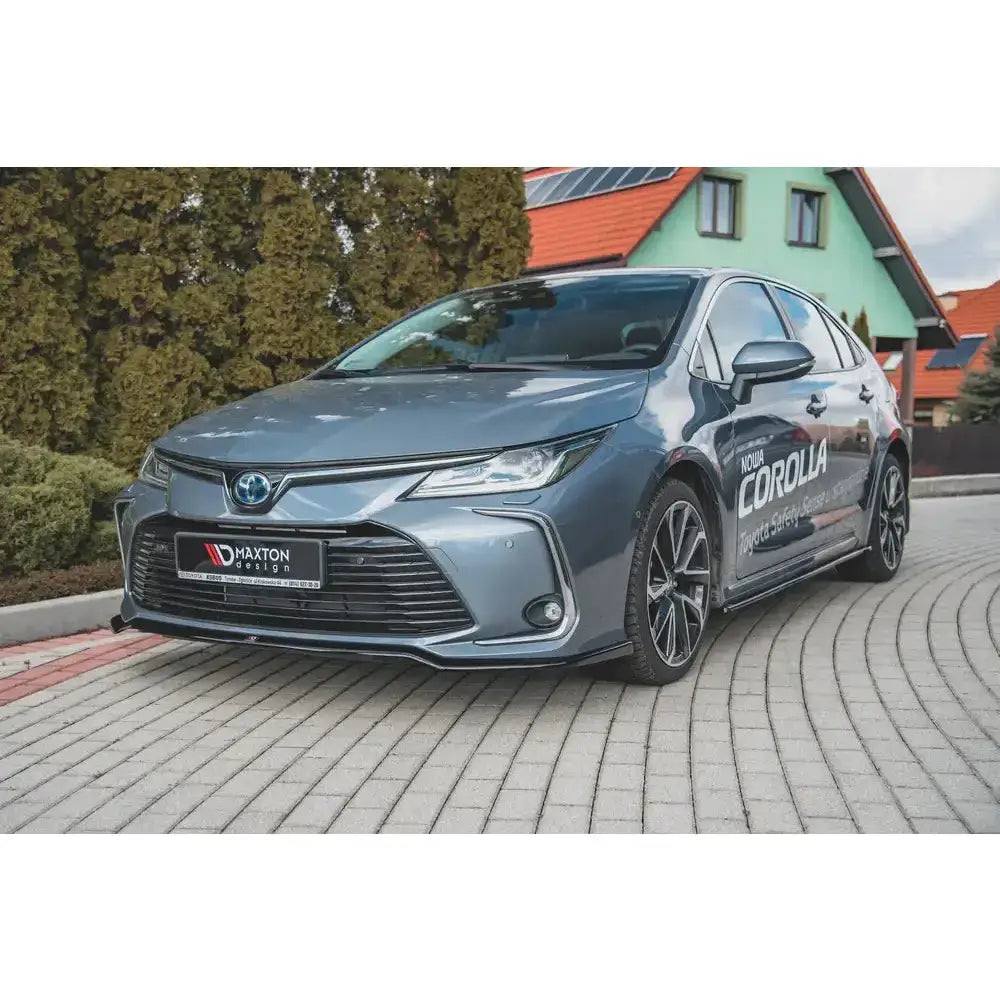Frontspoiler til Toyota Corolla XII Sedan med aluminiumsfelger og markert frontgrill, utendørs på brostein.