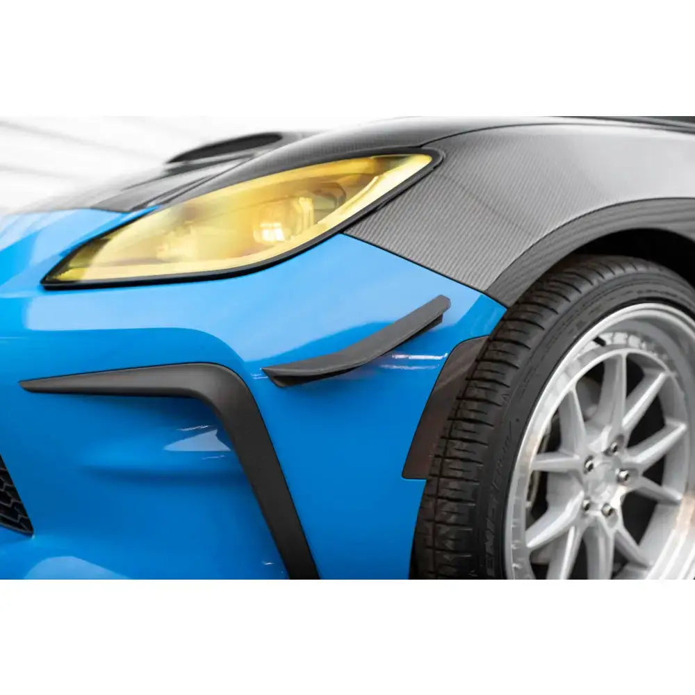 Frontsplitter på Toyota GR86 Mk1 med karbonfiberpanser, gult frontlys og svarte detaljer over venstre hjulbue.