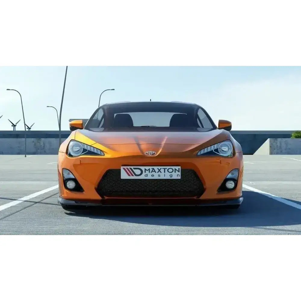 Frontsplitter på oransje Toyota GT86 med sorte detaljer og Maxton Design-logo foran på parkeringsplass.