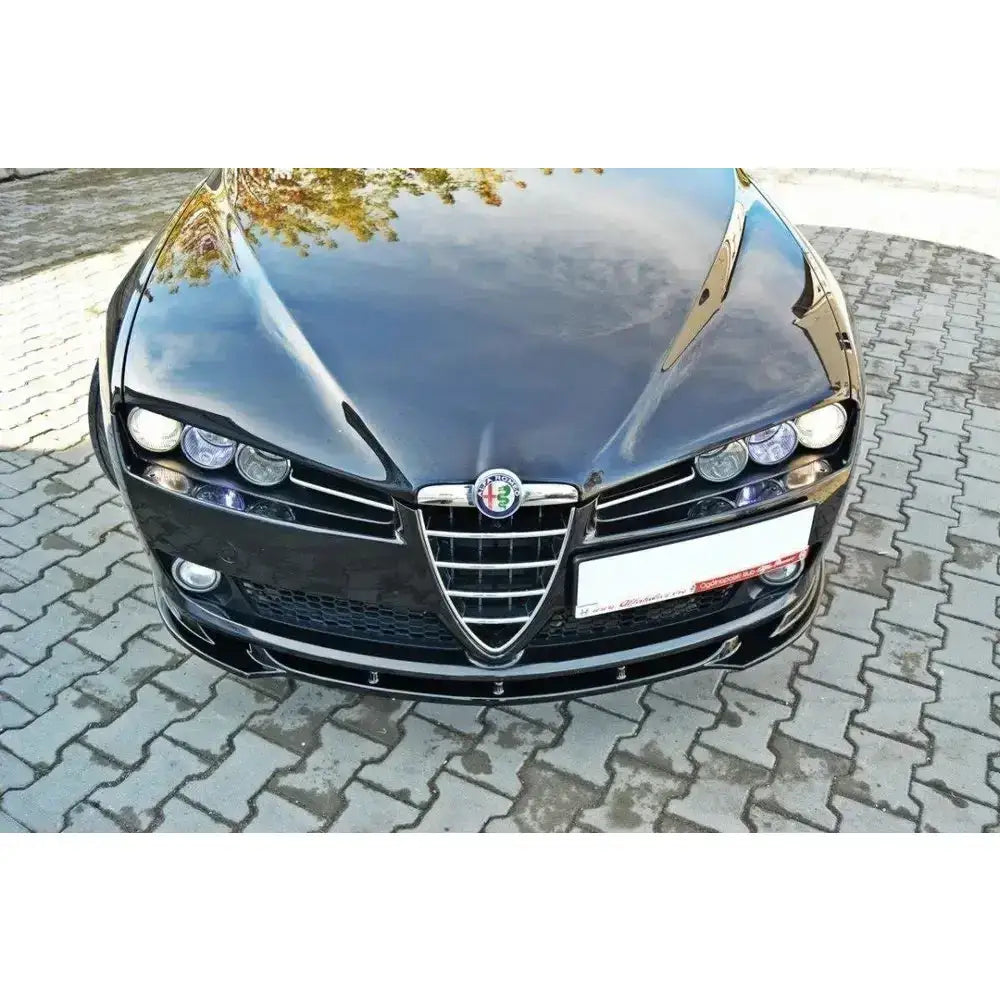 Frontsplitter på Alfa Romeo 159 vist forfra med sort grill og logo, parkert på steinbelagt bakke.