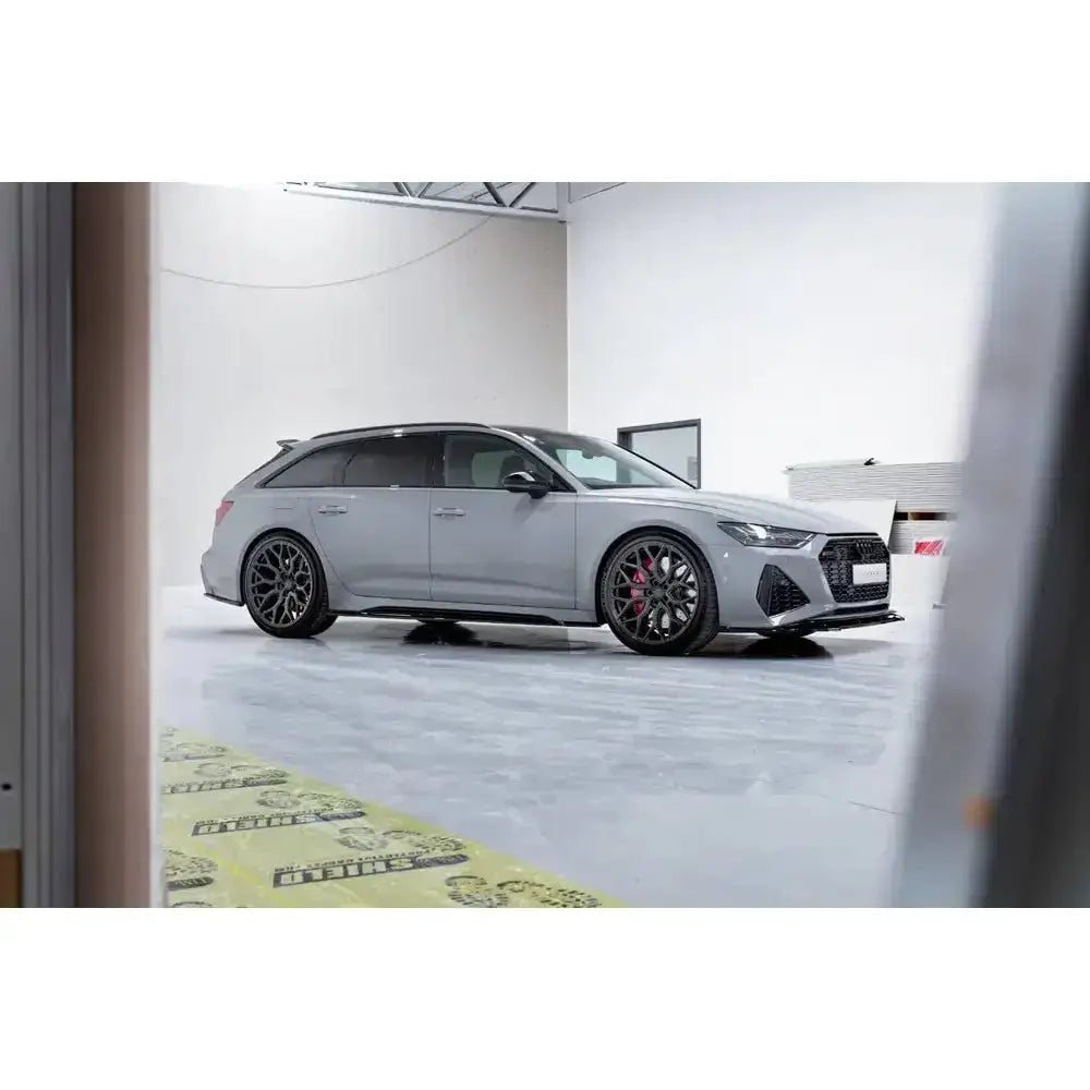 Frontleppe på grå Audi RS6 C8 stasjonsvogn med sorte felger og røde bremsekalipere i industrilokale.