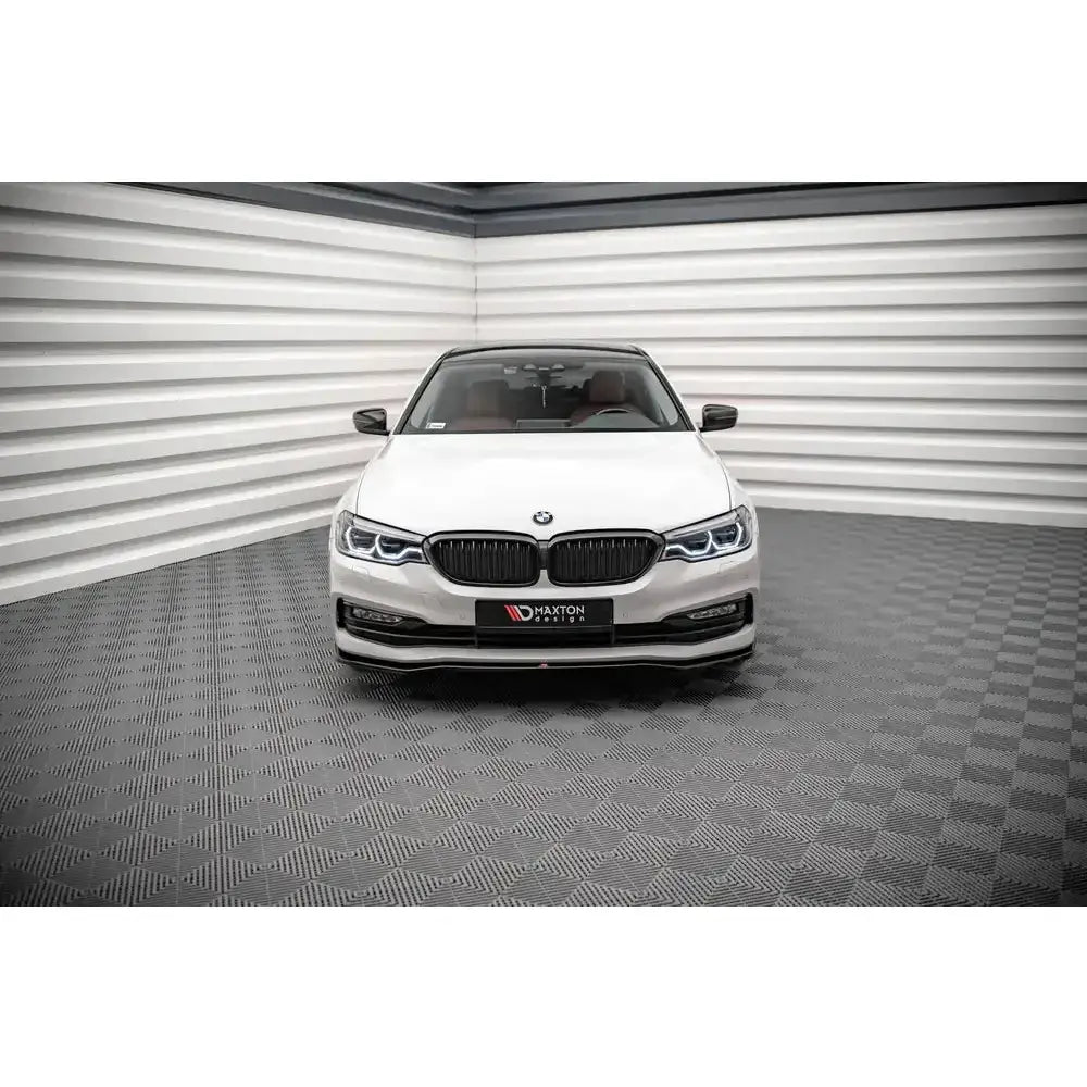 Frontspoiler på BMW 5-serie G30 17-20, hvit bil sett forfra i lyst showroom med mørkt gulv.