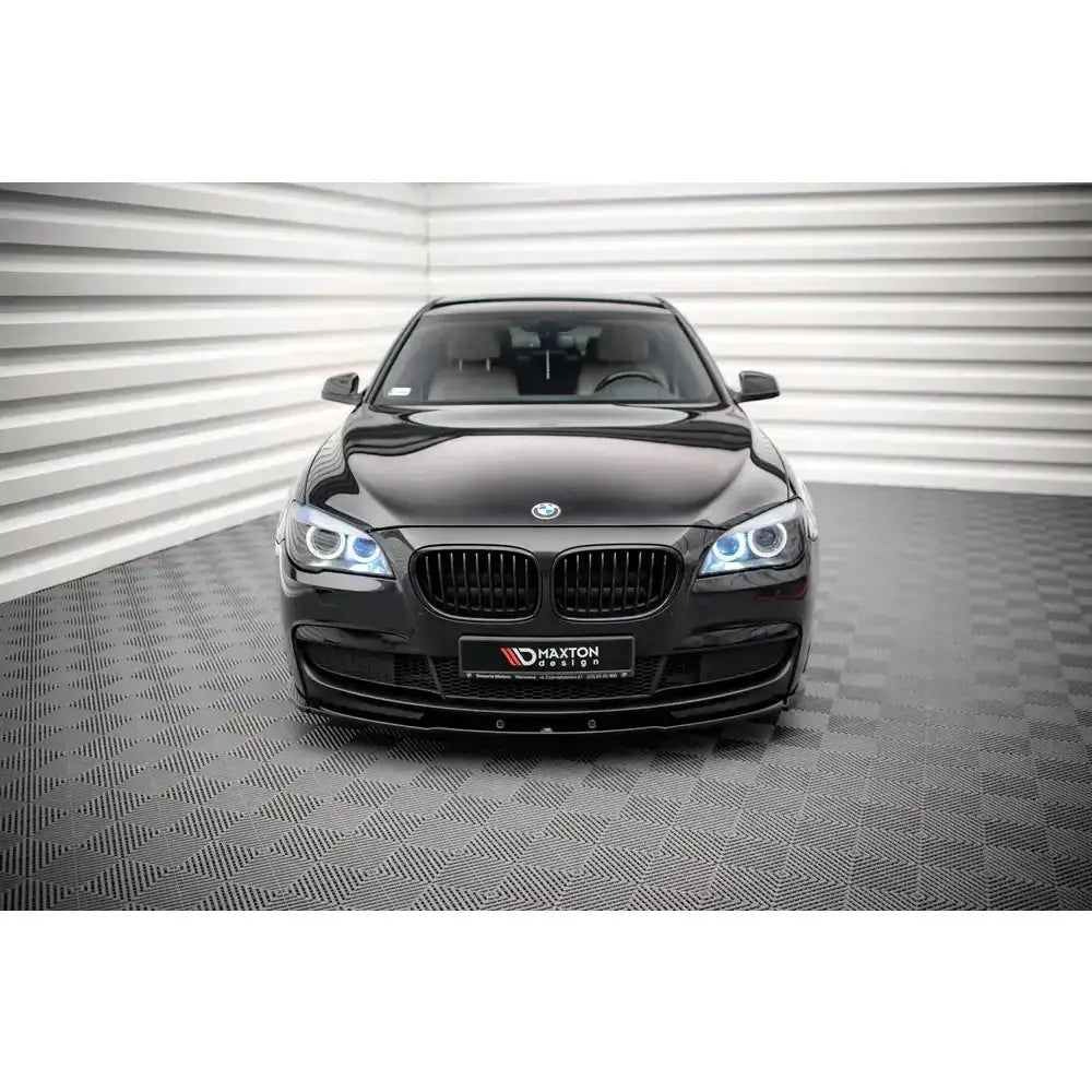 Frontsplitter på svart BMW 7 M-Pack F01 sett forfra med påslåtte frontlykter i lyst rom.