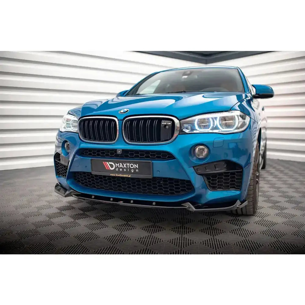 Front lip på blå BMW X5 M F15 14-18 med svarte detaljer og LED-lys, sett forfra på rutete gulv.