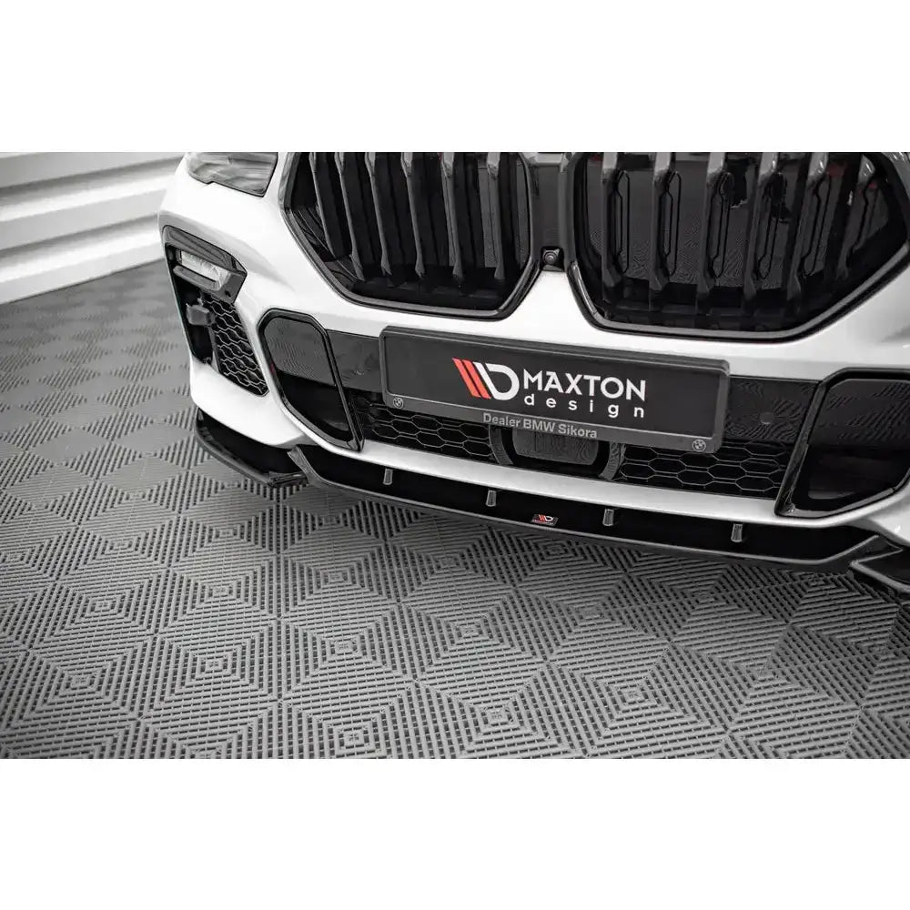 Front lip på Bmw X6 M-Pack G06 med sorte detaljer og spoiler, fotografert skrått forfra på mønstret gulv.