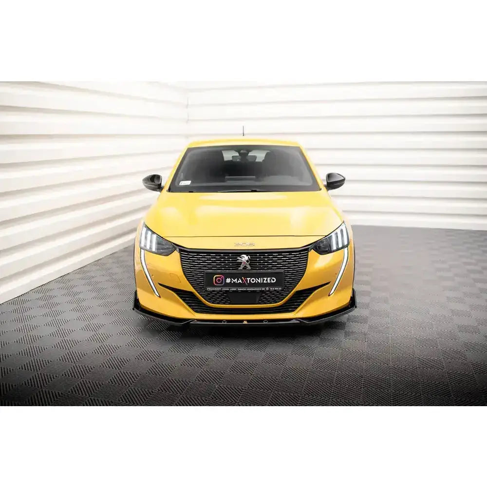 Frontspoiler på gul Peugeot 208 GT Mk2 med svart grill og LED-lys, fotografert forfra innendørs.