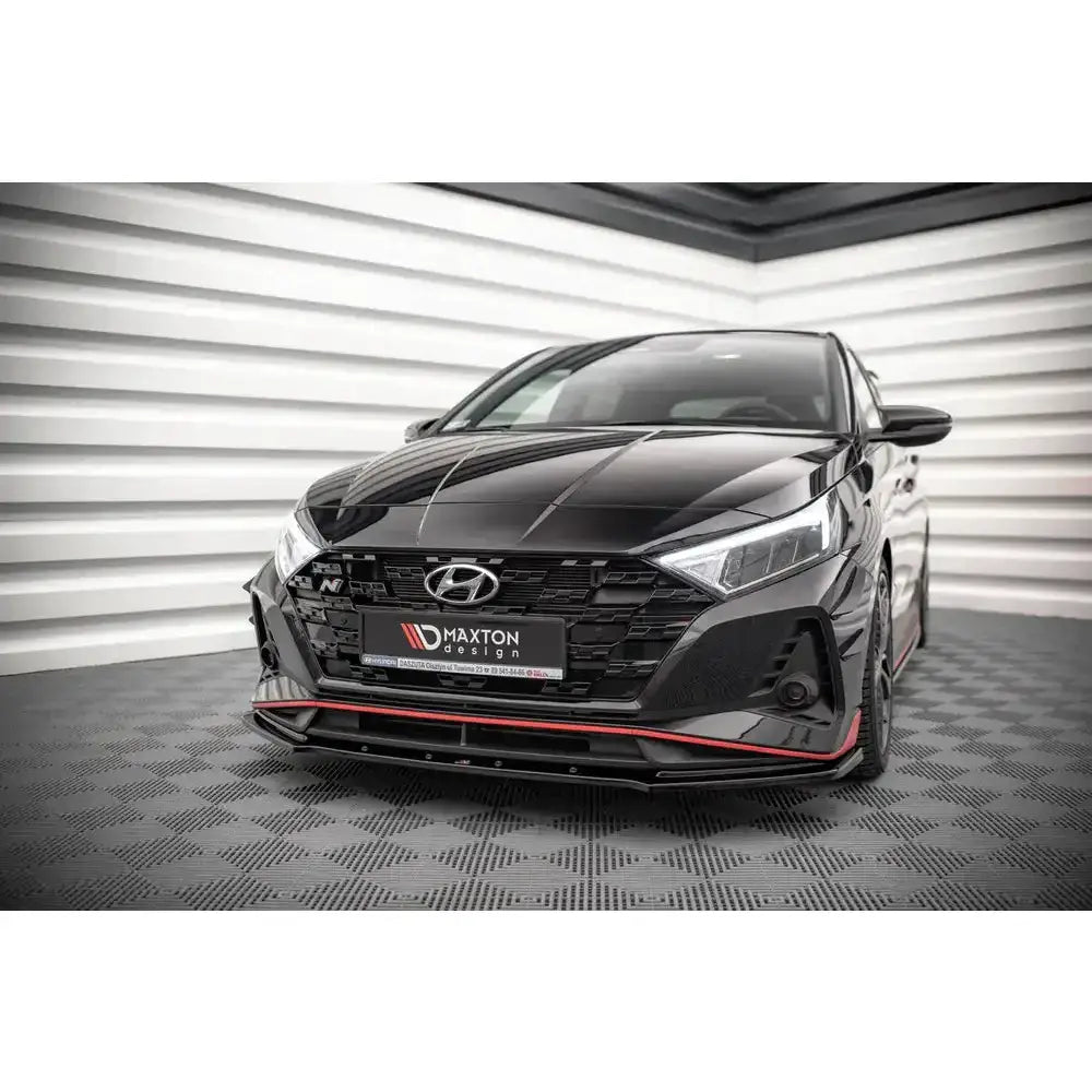 Frontsplitter på Hyundai I20 N Mk3 med røde detaljer, sett forfra på rutet gulv innendørs.