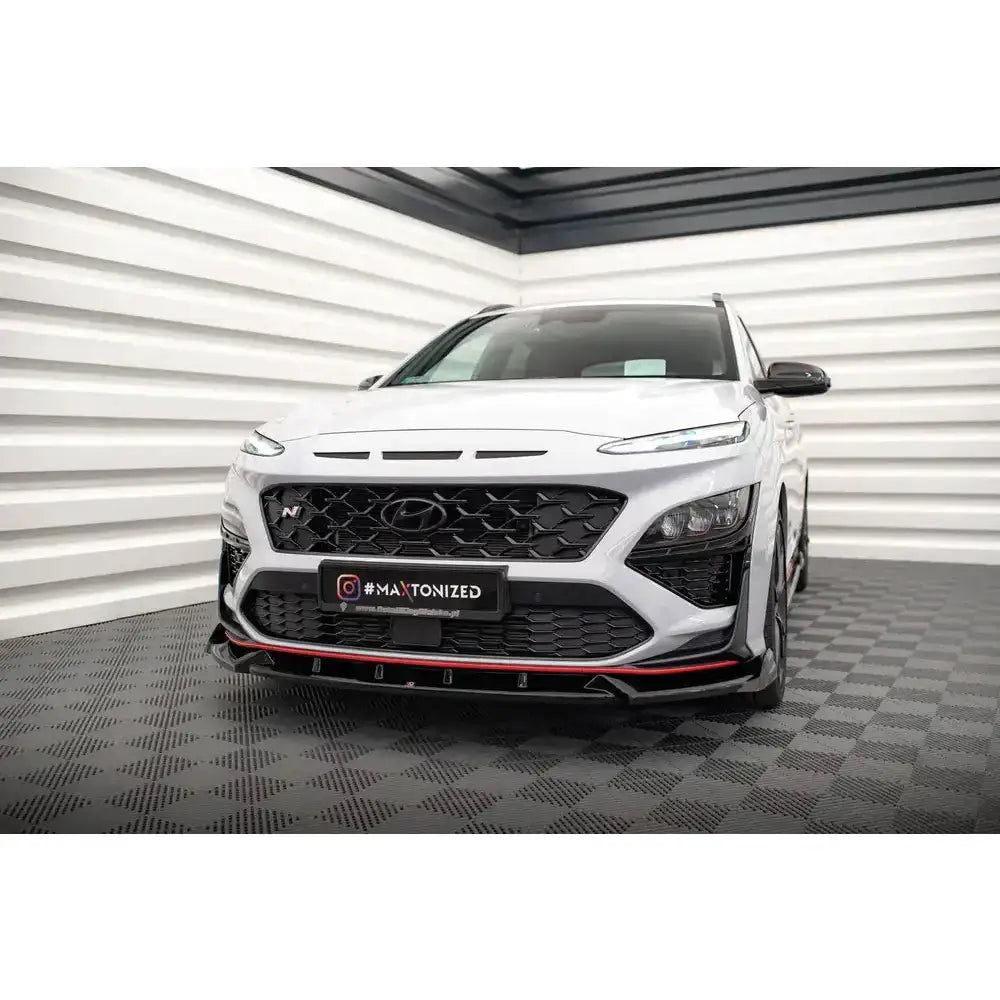 Frontspoiler på Hyundai Kona N Mk1 med svart grill og røde detaljer, sett forfra i lyst rom.