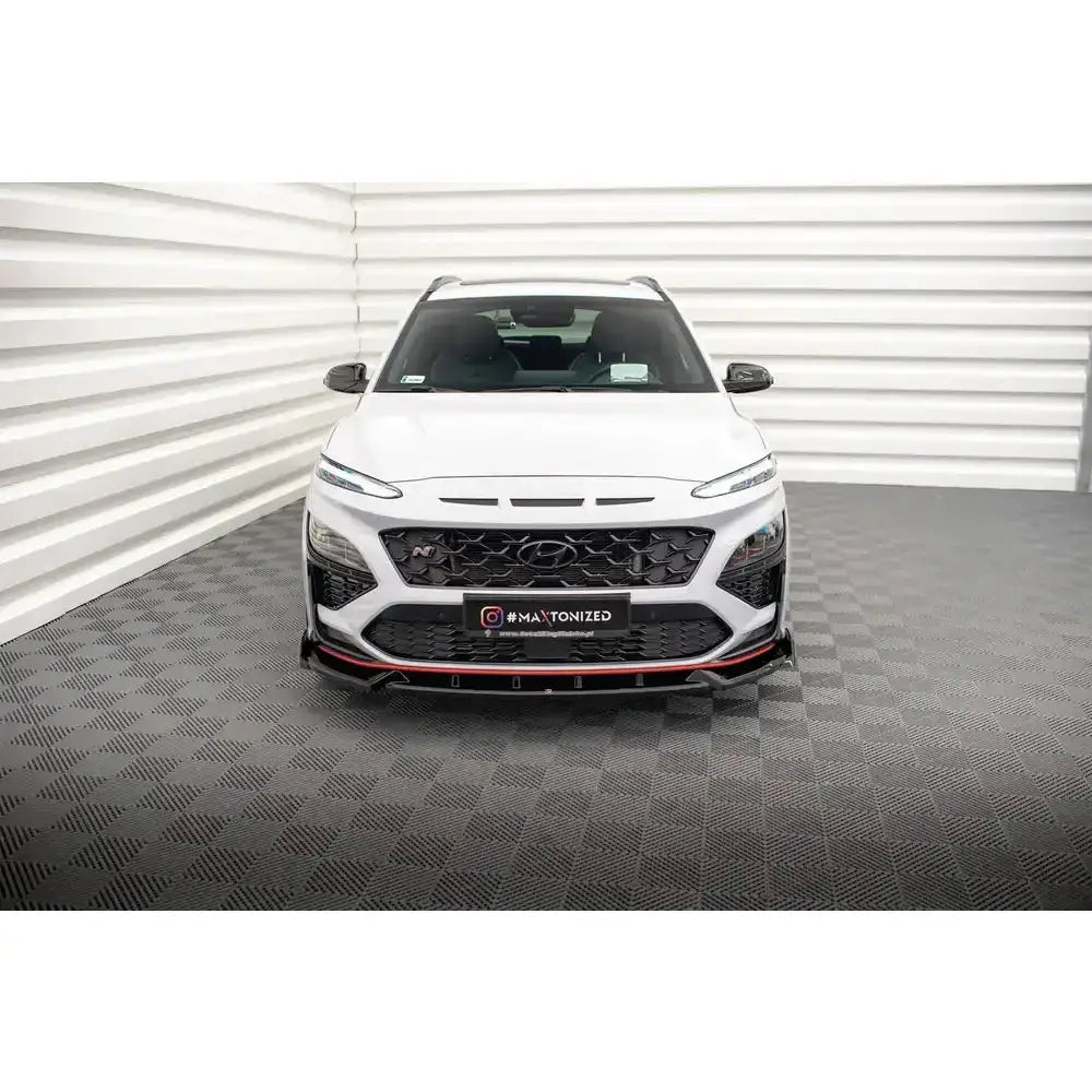 Front lip på Hyundai Kona N Mk1 i hvitt med svart og rød frontspoiler sett forfra innendørs.