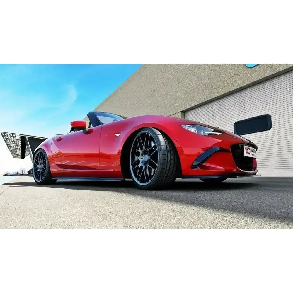 Frontsplitter på rød Mazda Mx-5 IV cabriolet med sorte felger og åpent tak foran en garasjeport.