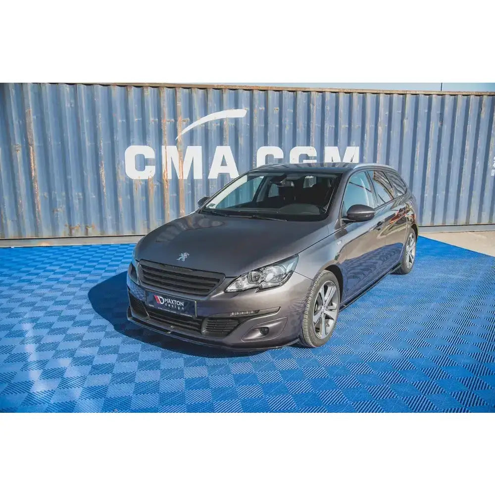 Frontspoiler på Peugeot 308 Mk2 Facelift med svarte detaljer, parkert foran container på blått underlag.