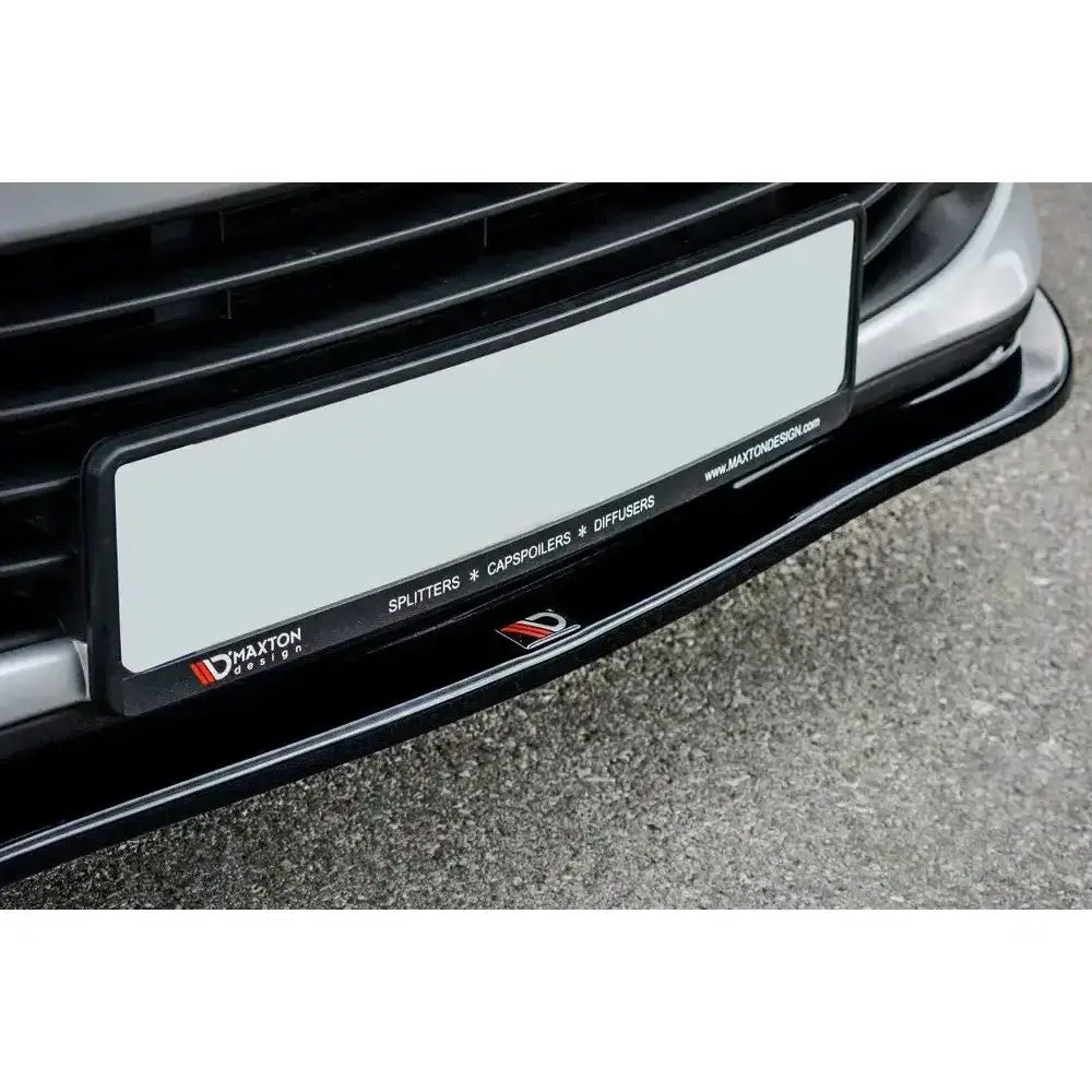 Frontspoiler til Renault Clio Mk4 V.1 i svart plast med synlige logoer, montert under frontfanger.