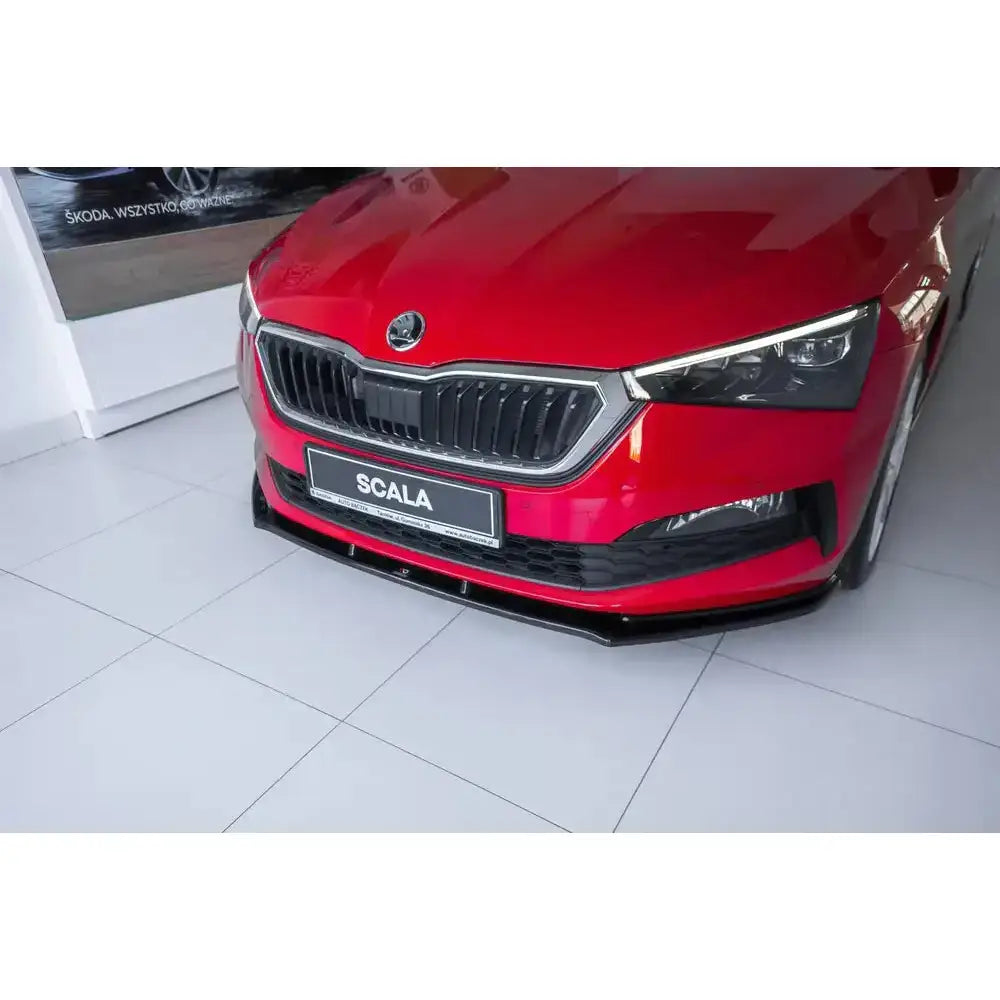 Frontsplitter på Skoda Scala V.1, sort plast under rød bils front, sett fra skrå vinkel innendørs.