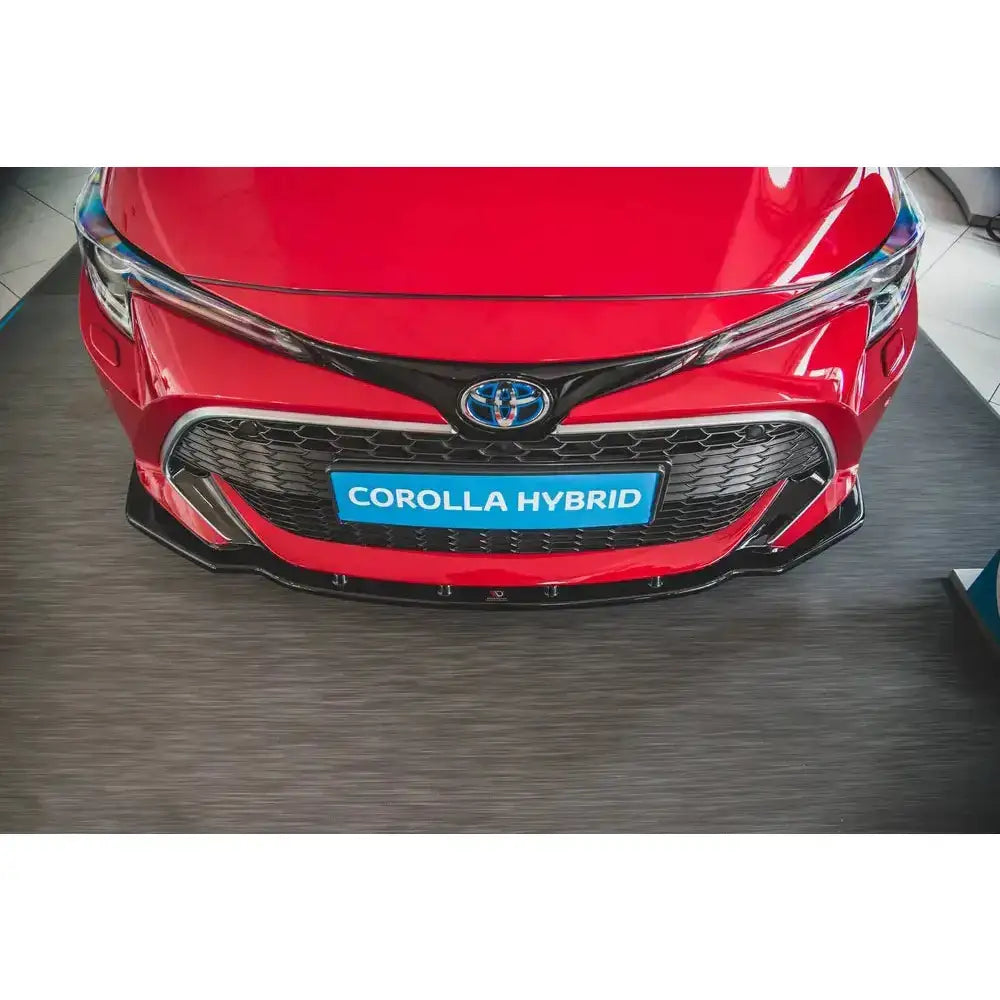 Frontspoiler på rød Toyota Corolla XII med sort grill, blå logo og skiltet "COROLLA HYBRID" foran.