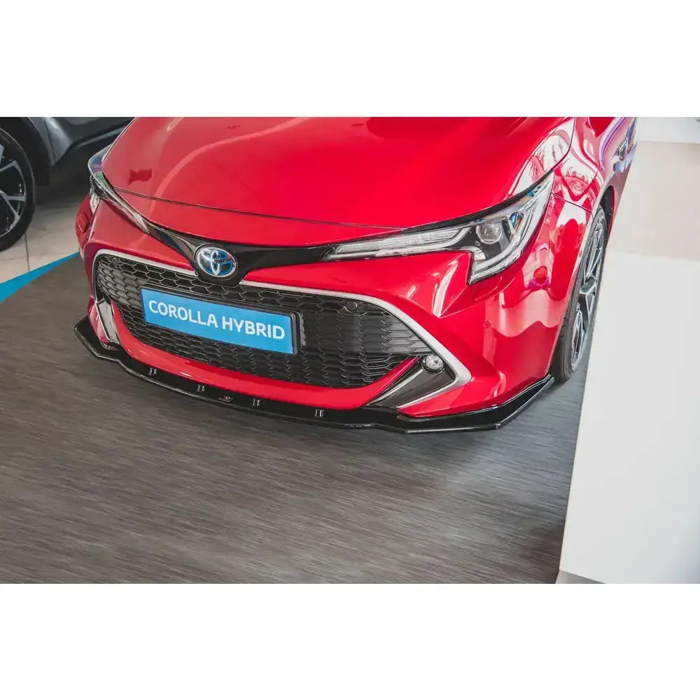 Frontsplitter på rød Toyota Corolla XII med sort grill, blått hybridskilt og sort frontspoiler.