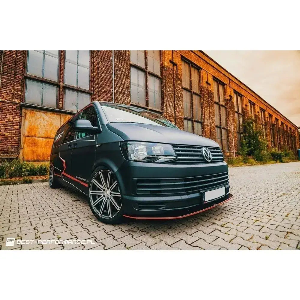Front lip Volkswagen T6 sort varebil med sølvfelger og røde dekorlinjer foran murbygning.