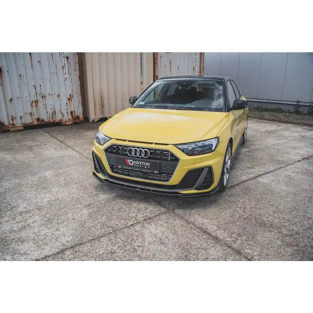 Front splitter på Audi A1 S-Line GB i gul med sorte detaljer, parkert foran rustne containere.