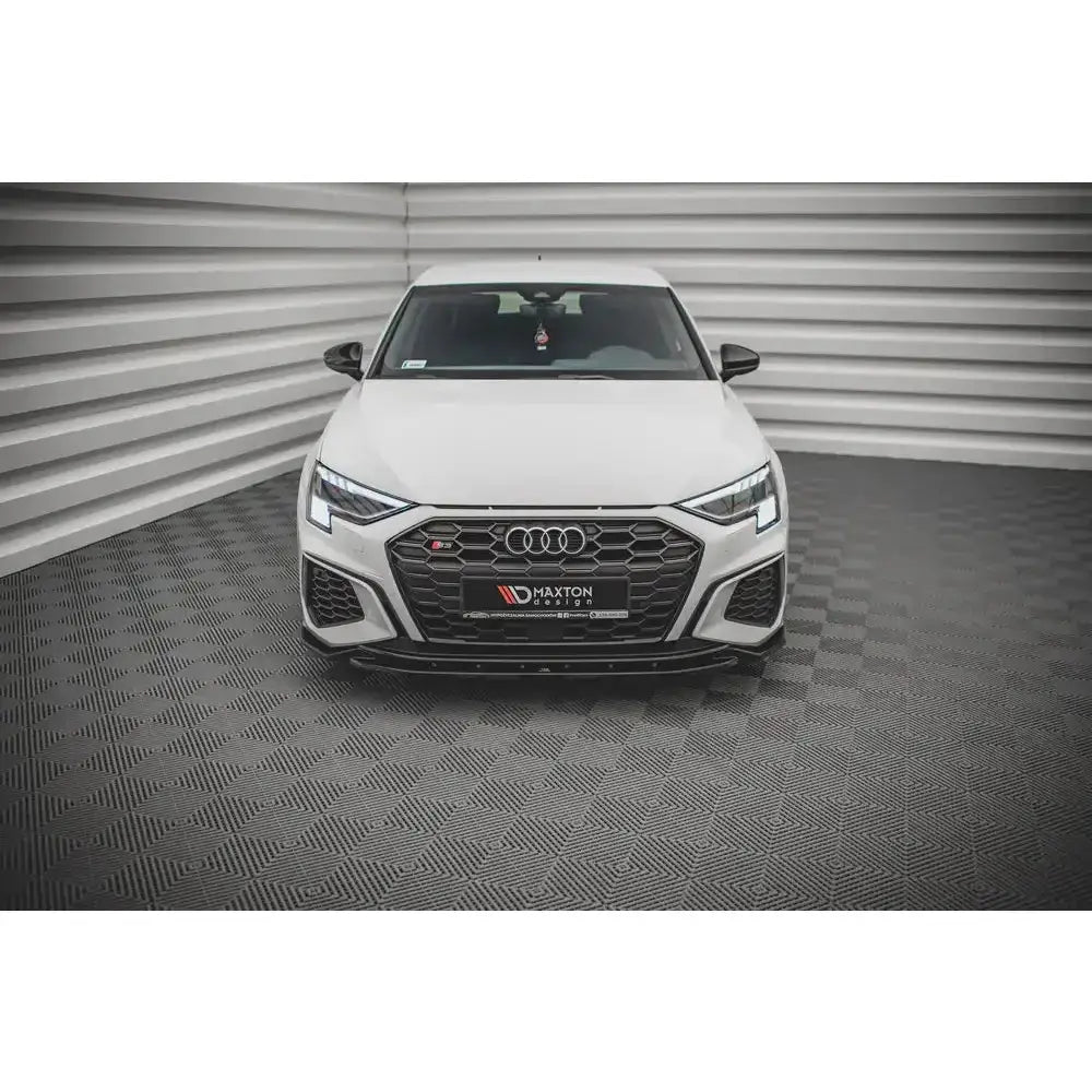 Frontspoiler på hvit Audi S3 med sort grill, LED-lykter og sportslige detaljer, sett forfra innendørs.