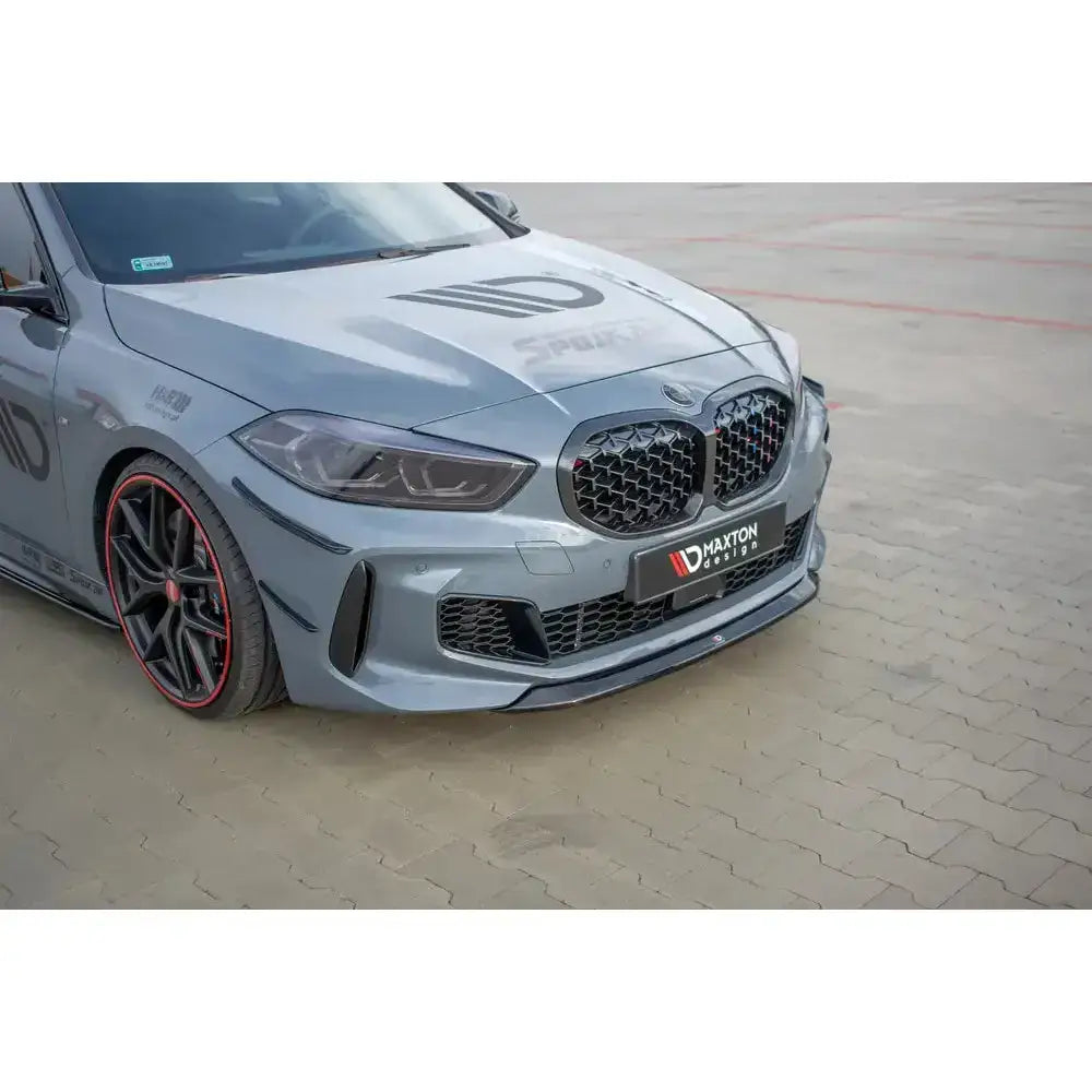 Front lip på BMW 1 F40 M-Pack med svart grill, rød felgkant og sporty detaljer, parkert på lys stein.
