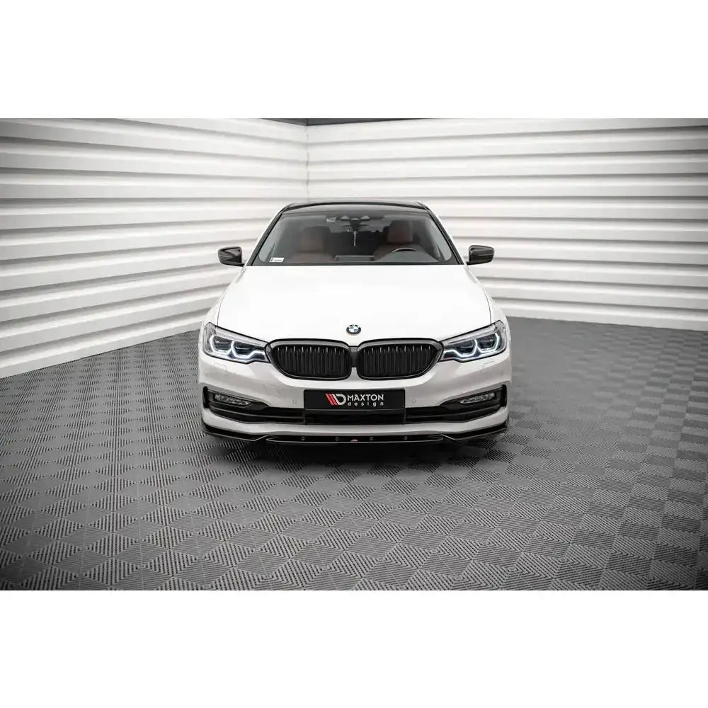 Frontspoiler på hvit BMW 5 G30 V.2 sett forfra med sorte detaljer og LED-lys, inne i lyst rom.