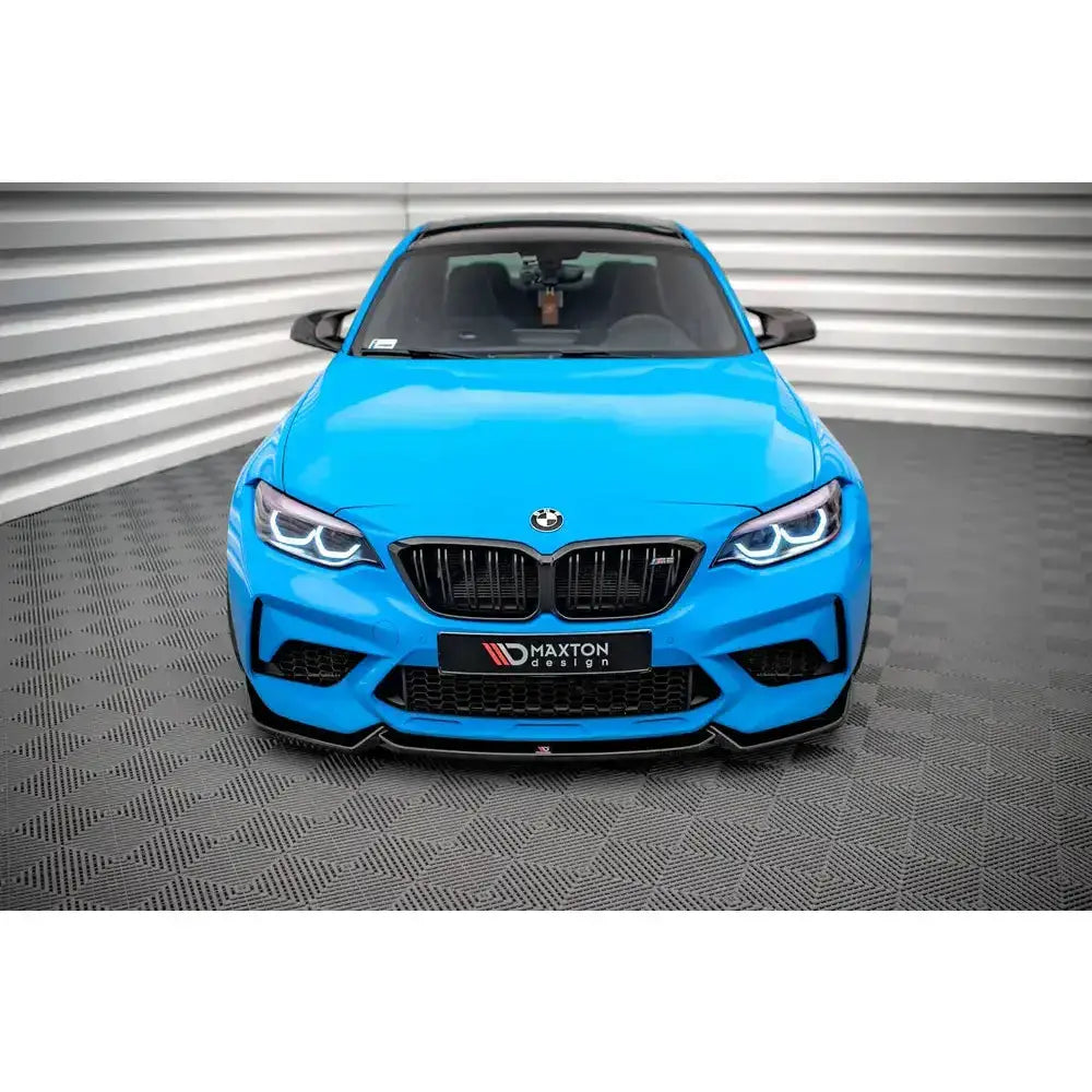 Frontspoiler på blå BMW M2 Competition F87 med sorte detaljer, sett forfra på rutemønstret gulv.