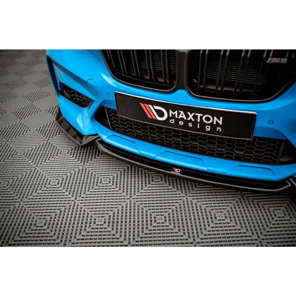 Frontsplitter på BMW M2 Competition F87, nærbilde av sort frontleppe i blank finish mot rutete gulv.
