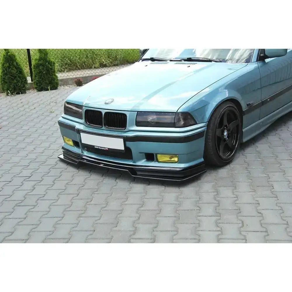 Frontspoiler på BMW M3 E36 V.2 i lyseblått med svart leppe og gule tåkelys på grå belegningsstein.